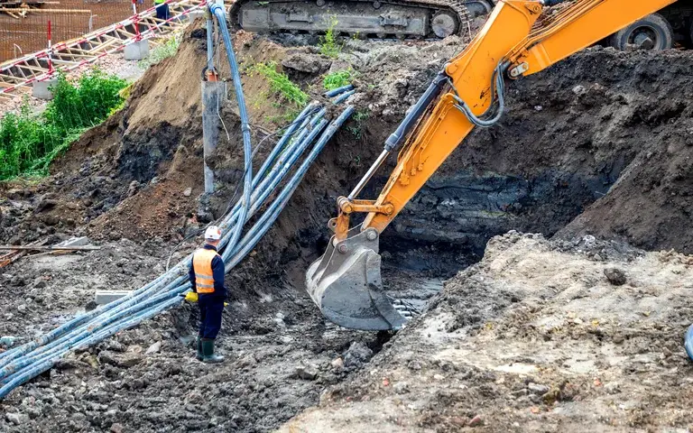 Glasfaser- und Leitungsbau: Bagger am offenen Kabelgraben